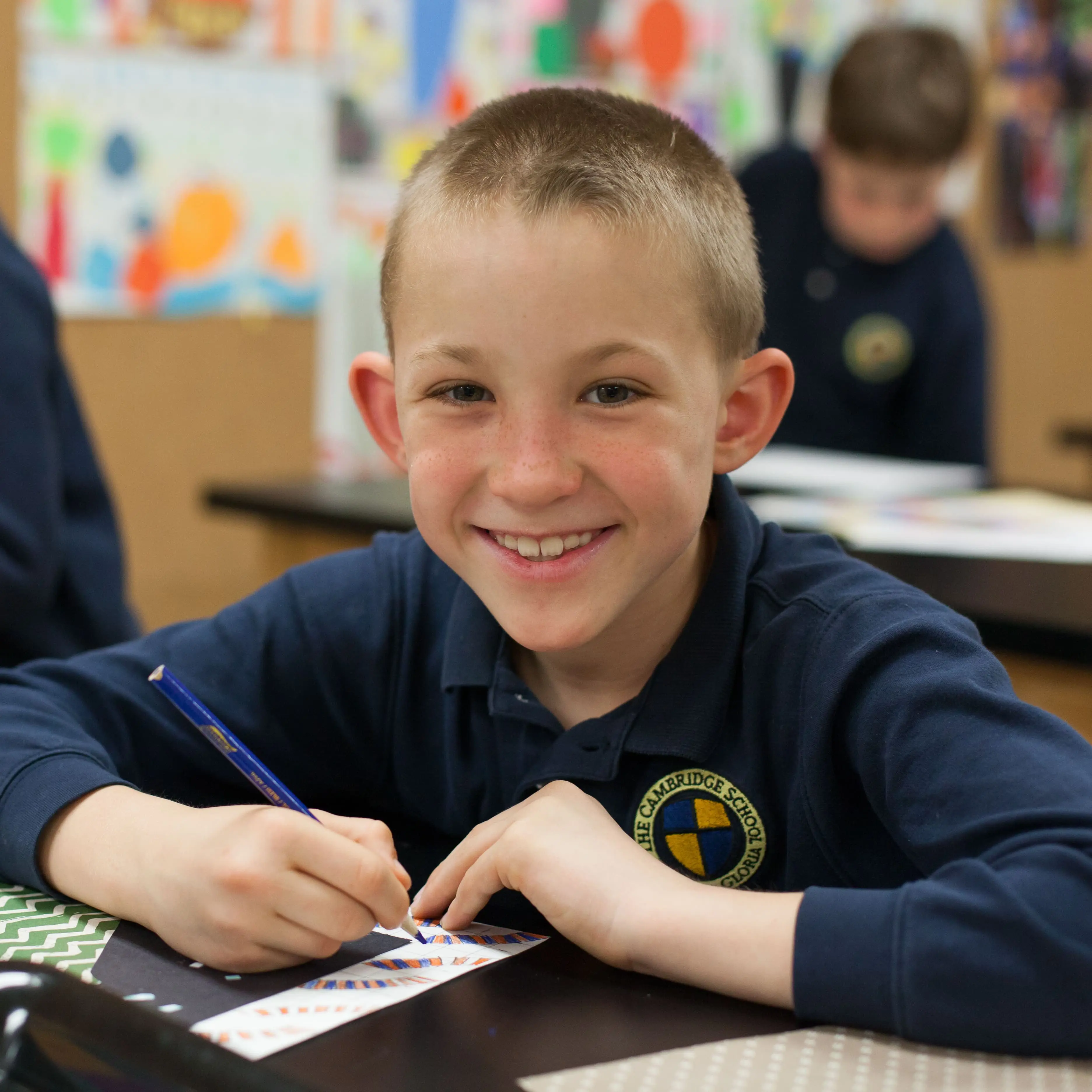 smiling young students looks up from his art project to smile for the camera.