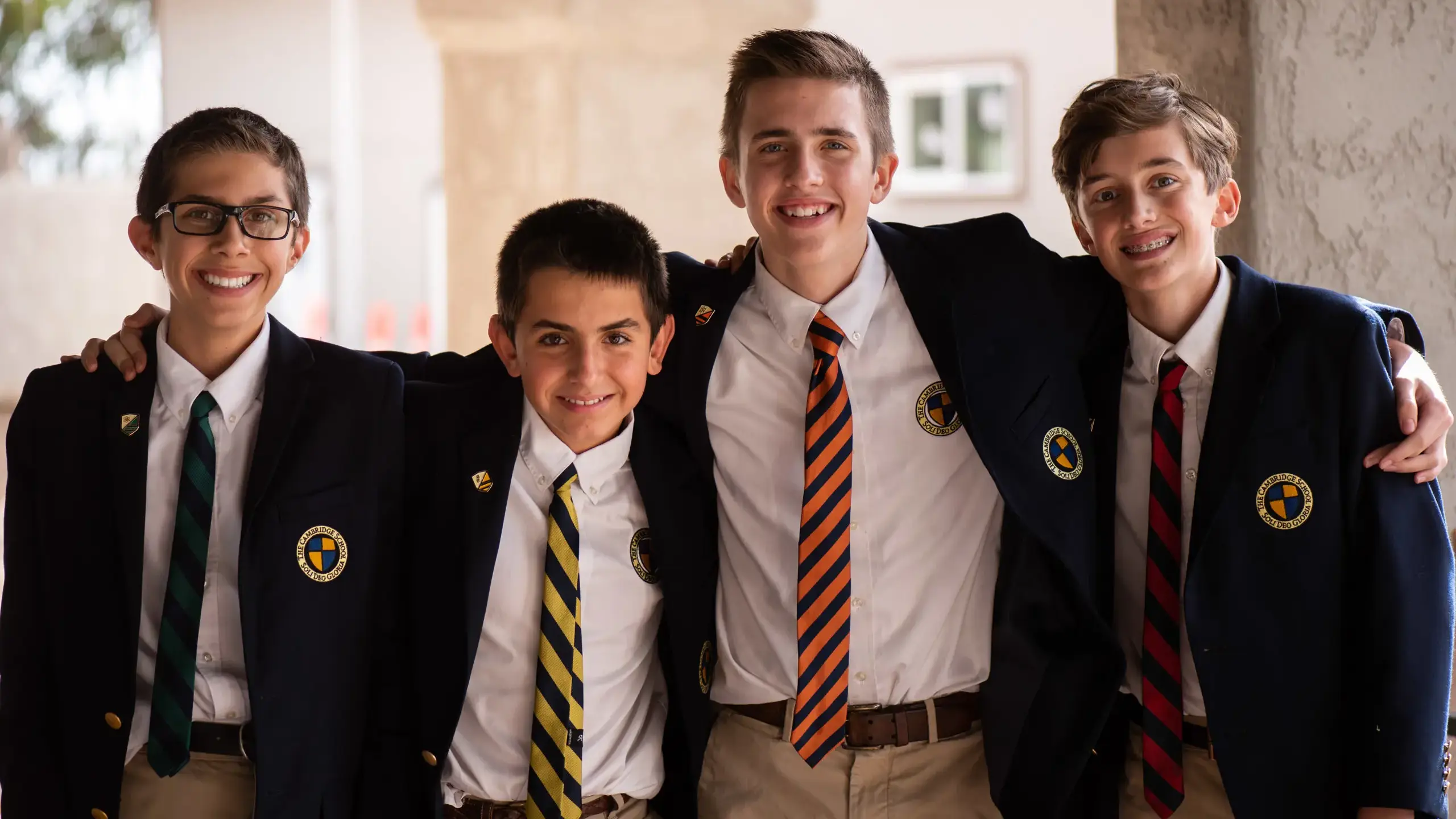 Four smiling Cambridge School students in blazers and house ties stand together, reflecting the strong sense of community and camaraderie fostered within the school.
