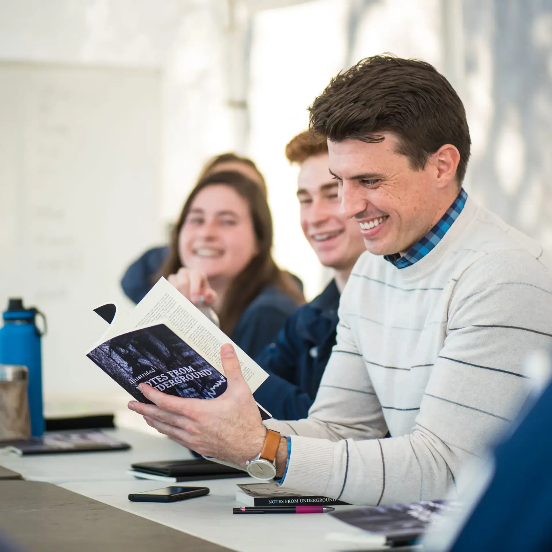 Group sitting at table and smiling as they read a book