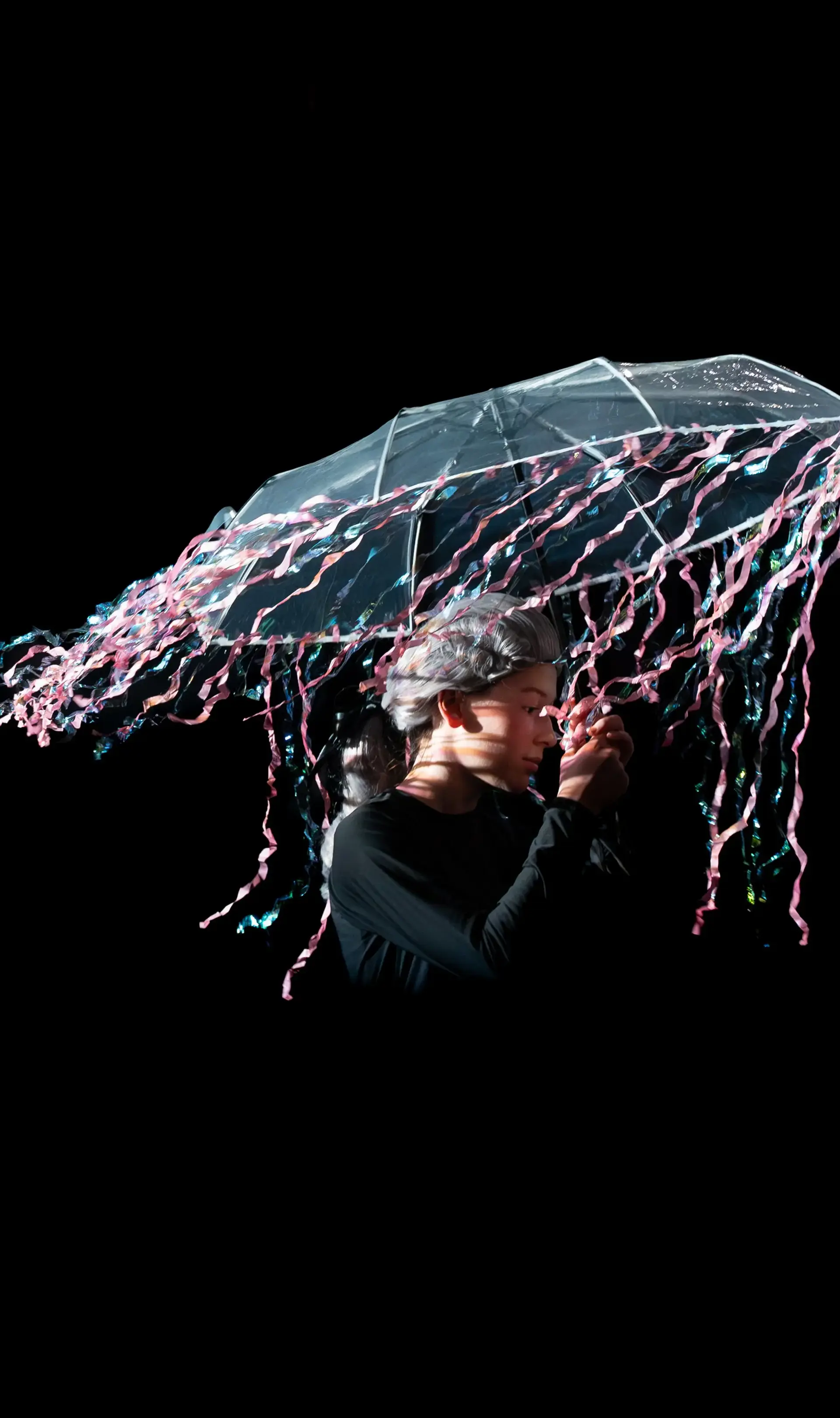 Student standing against black backdrop holding up an umbrella with pink streamers hanging from it