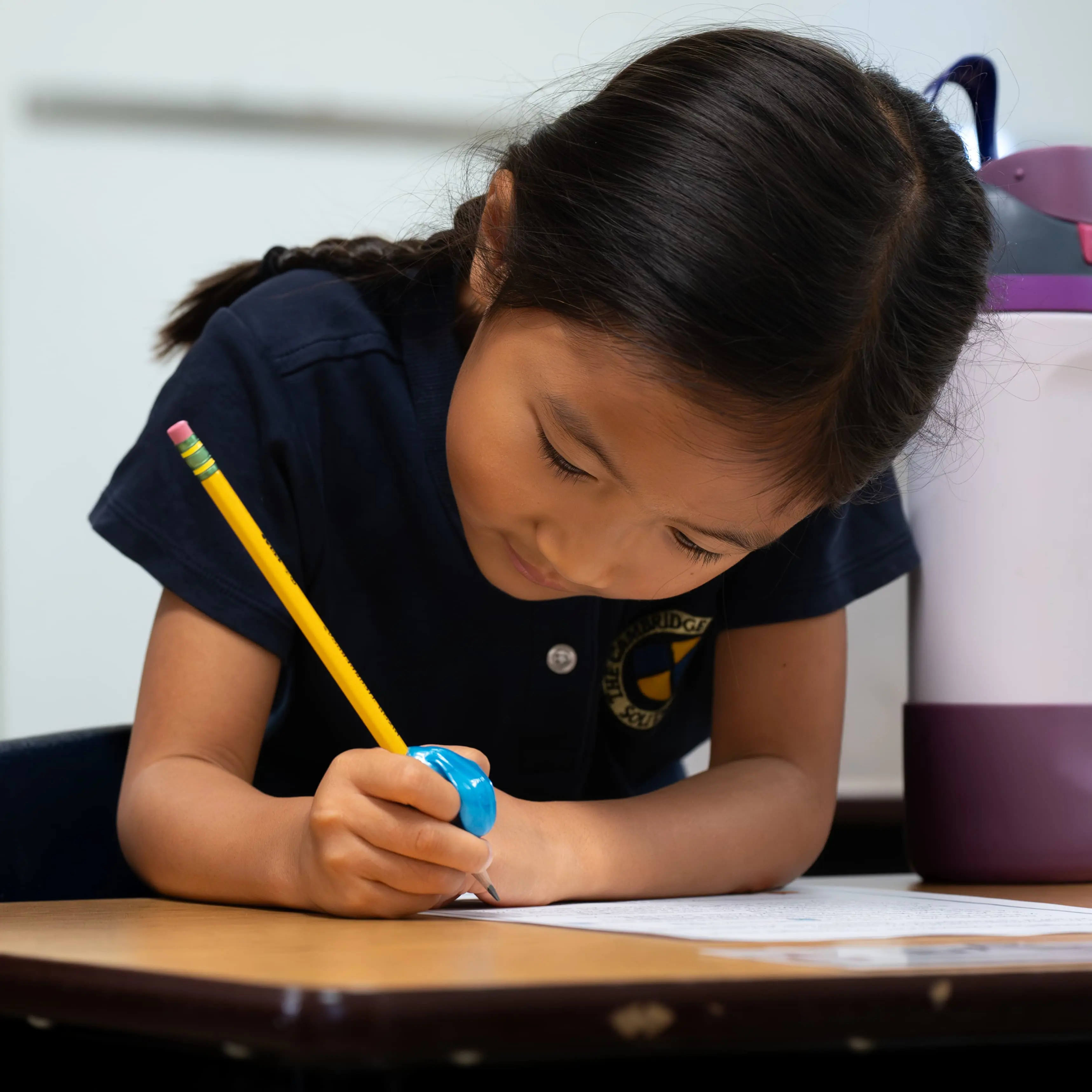 A focused Cambridge School student meticulously completes school work at a desk with a pencil.