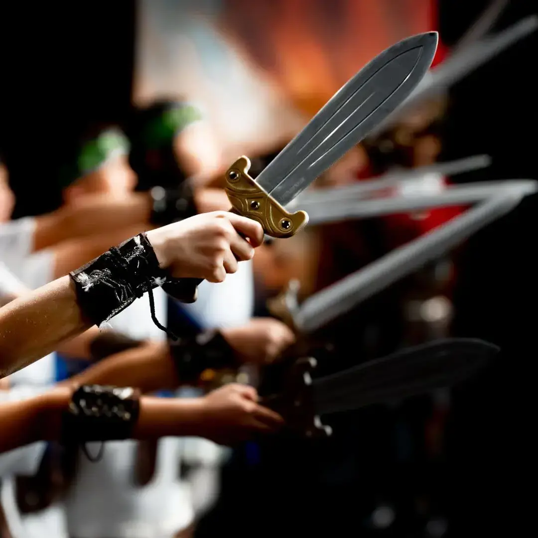Cambridge students in costume raise their swords during a dramatic reenactment of the Trojan War, bringing ancient literature to life through an immersive classroom performance.