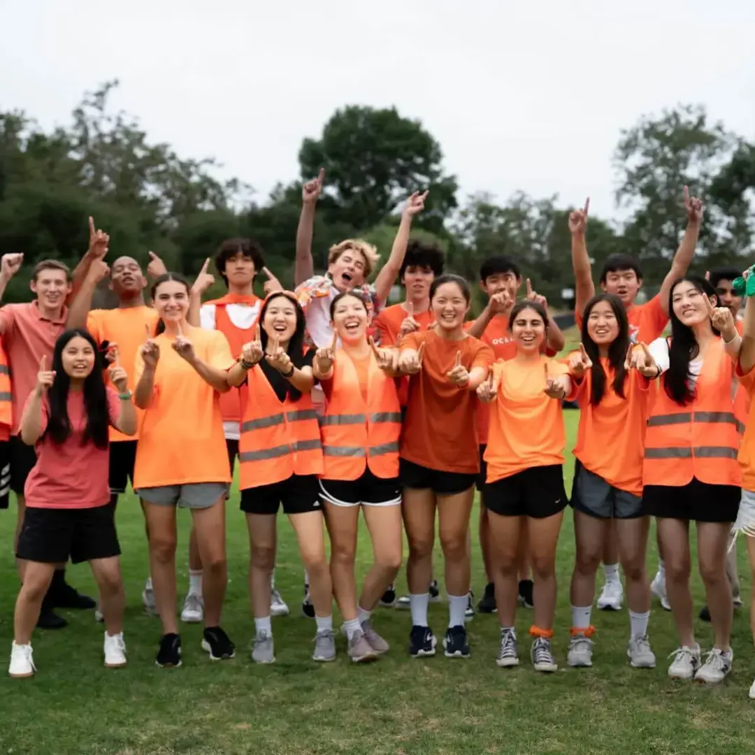 Cambridge upper school students wearing bright orange cheer and celebrate together on the field during a House competition, showing school spirit and camaraderie.