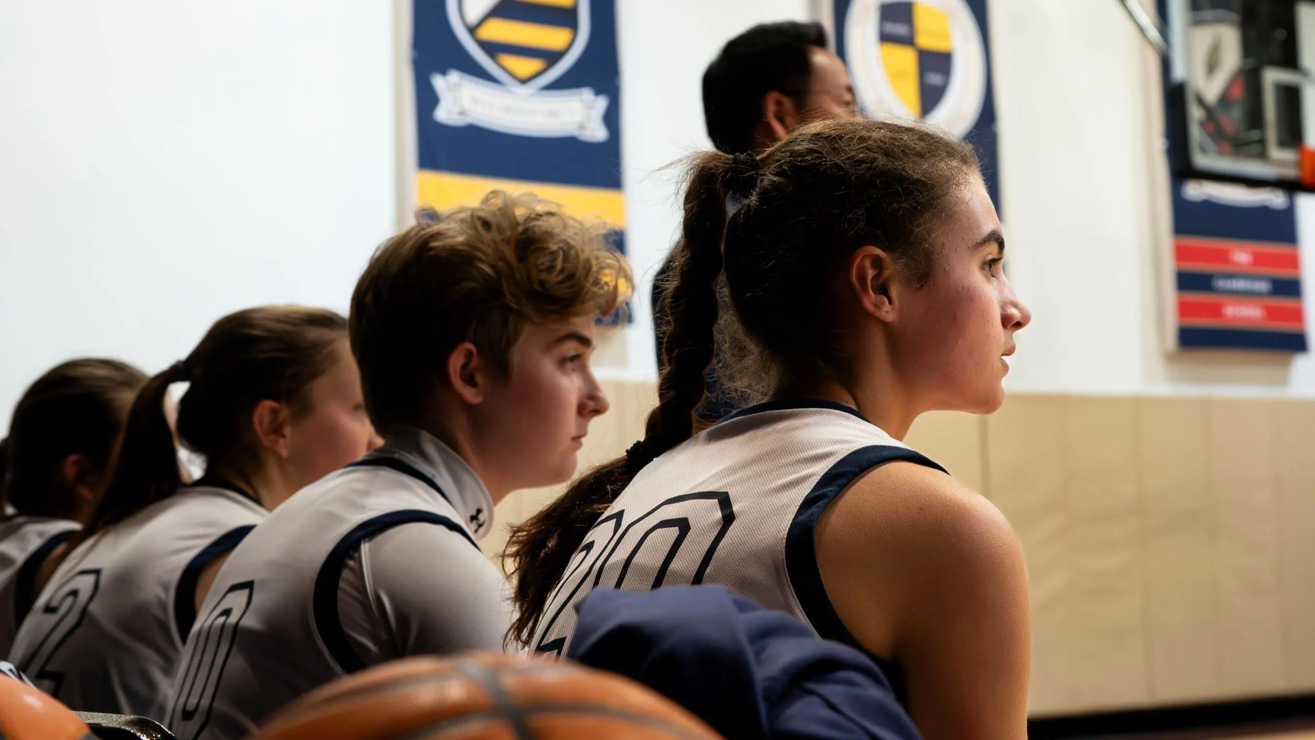 Cambridge student-athletes sit focused on the bench during a basketball game, embodying discipline, teamwork, and character formation beyond the classroom.