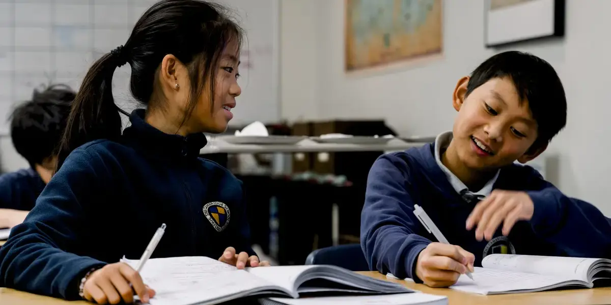 Two Cambridge School students in uniform engage in a classroom.