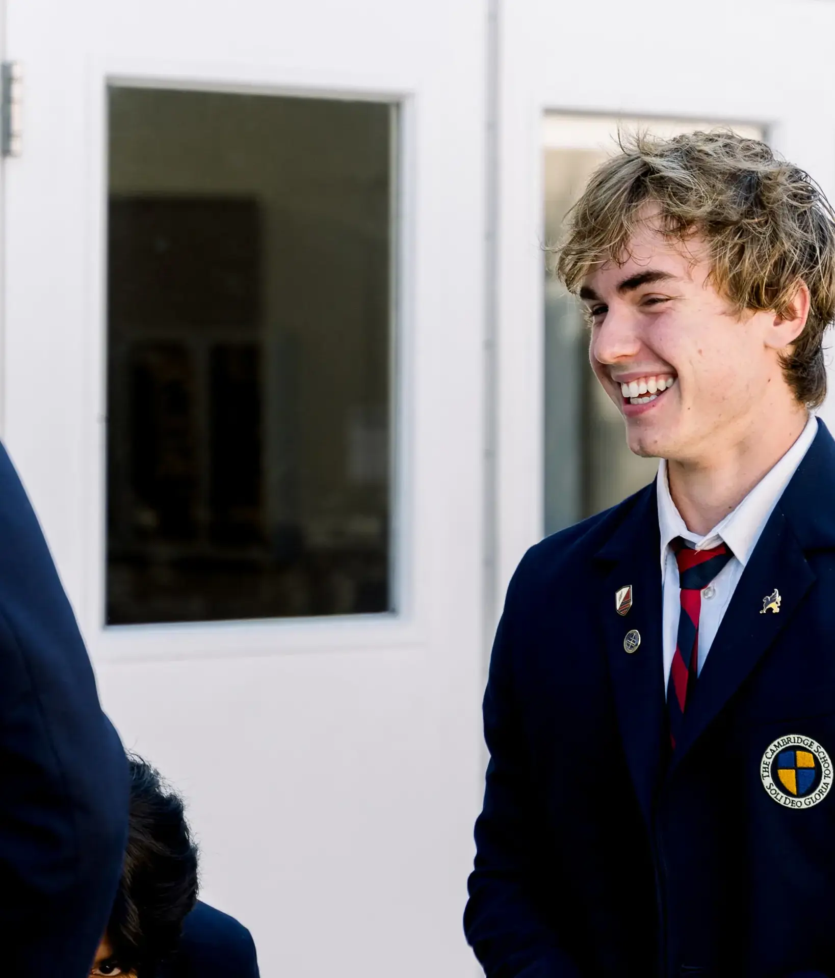 A Cambridge School student, wearing a blazer adorned with pins, shares a joyful moment with a classmate
