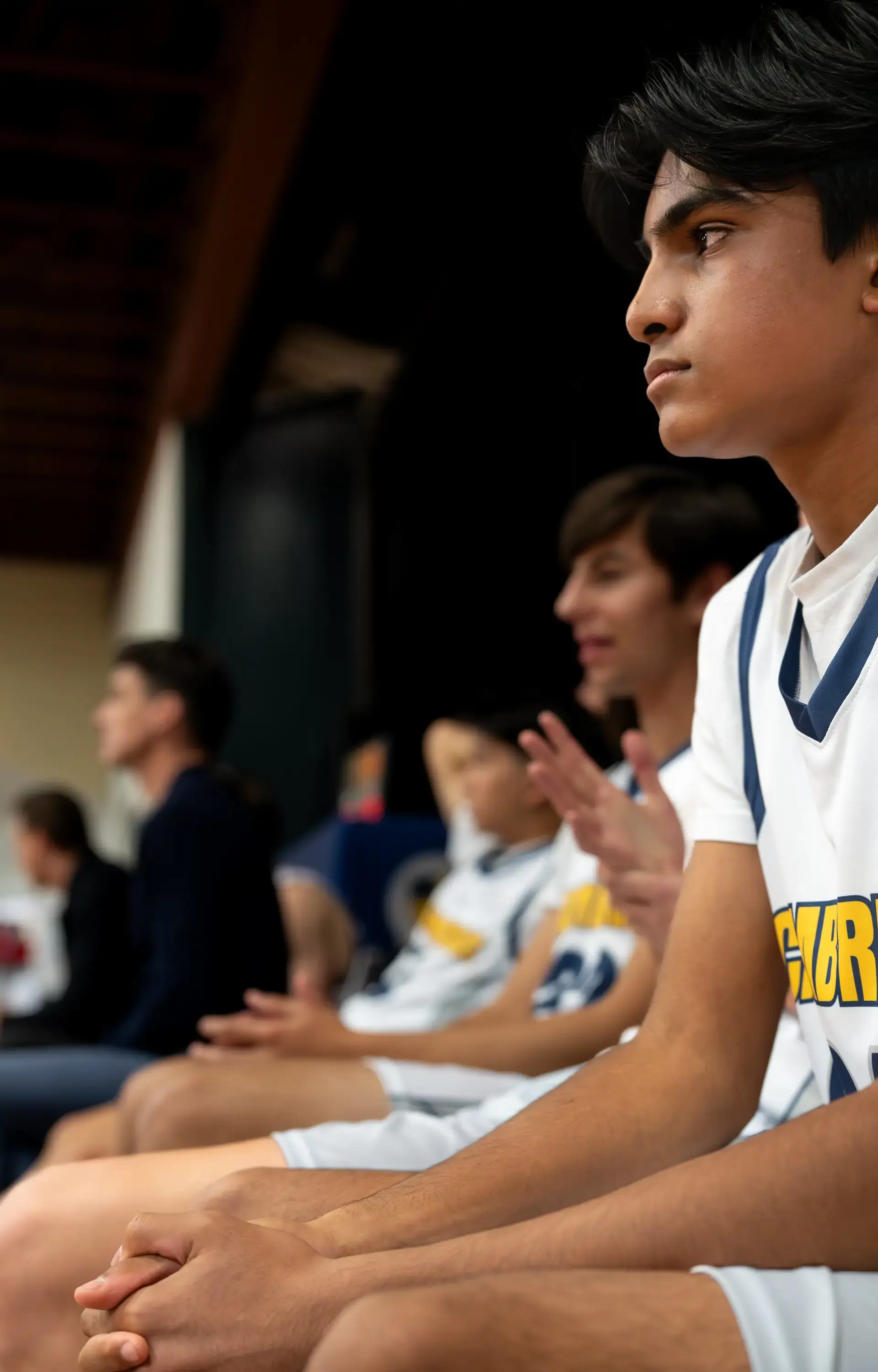 A Cambridge Griffins basketball player sits on the sideline in quiet focus during a home game.
