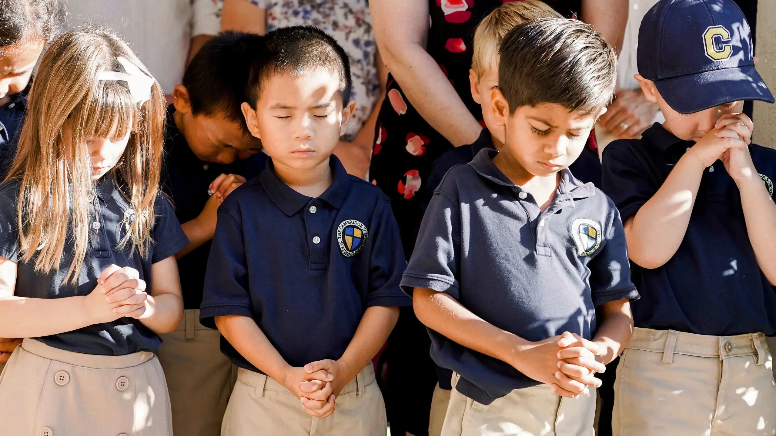 Cambridge School students with bowed heads and clasped hands engage in a moment of prayer or reflection
