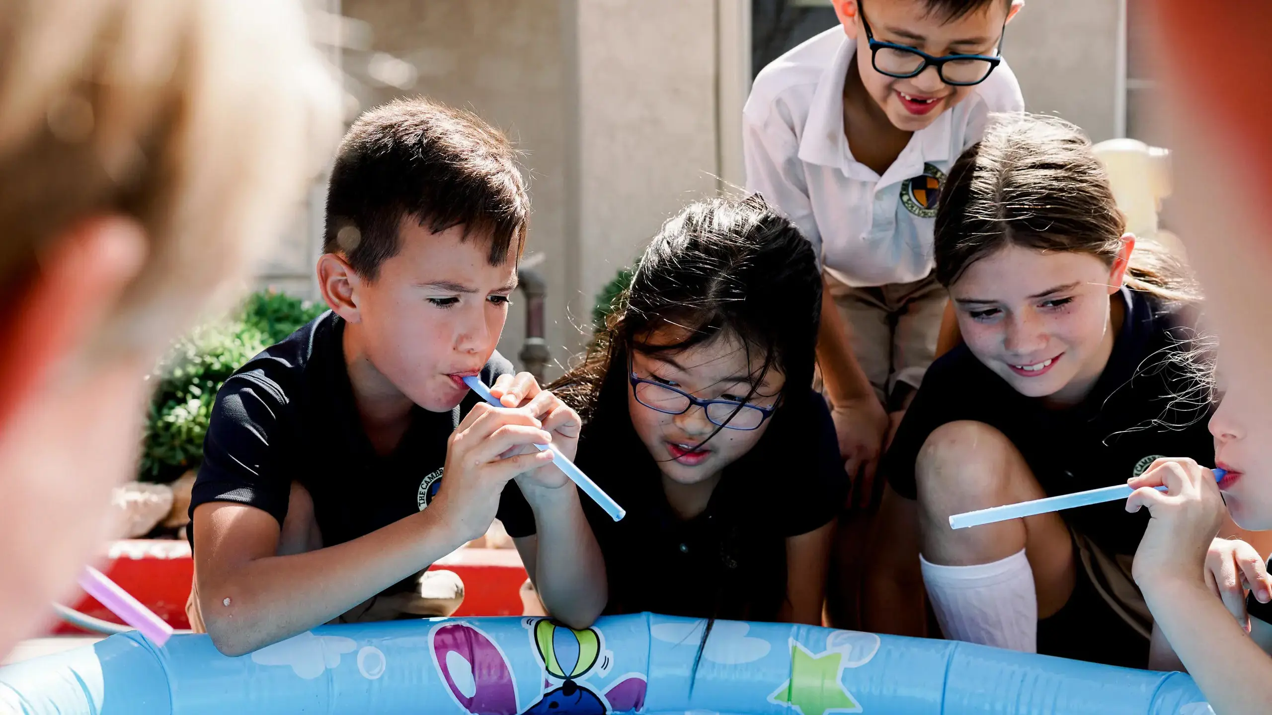 Cambridge School students engage in a hands-on discovery activity around a small pool.
