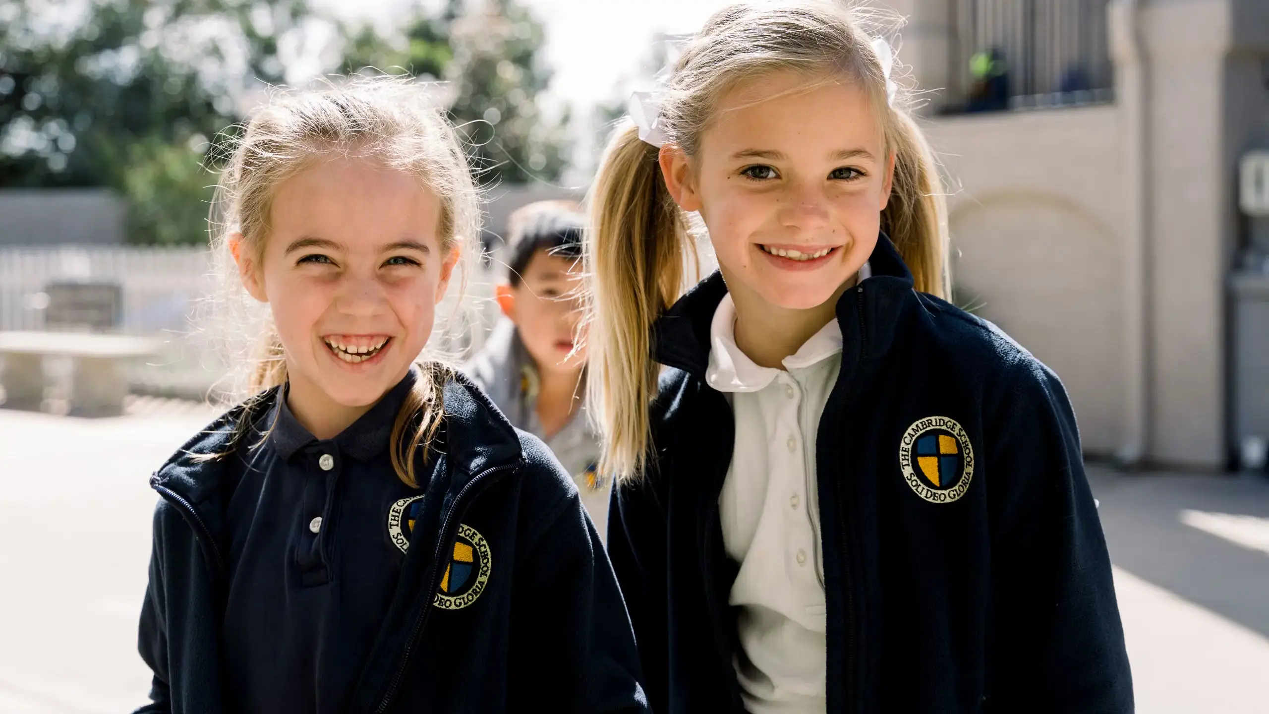 Two smiling elementary-aged girls in Cambridge School jackets.