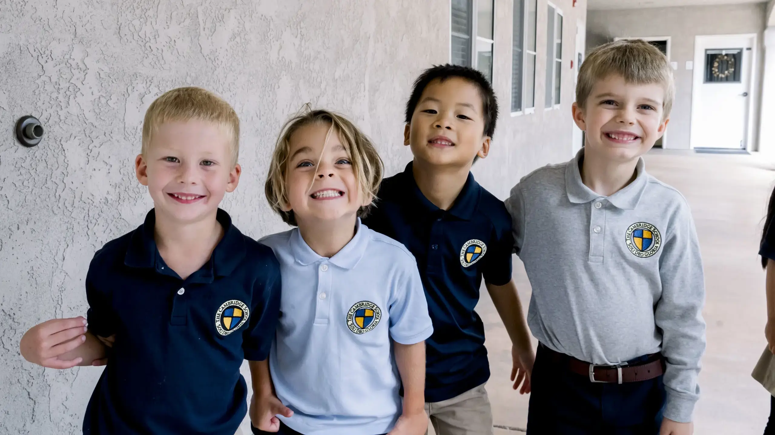 Four Kindergarten boys at The Cambridge School, a private classical Christian school in San Diego, smile joyfully in uniform.