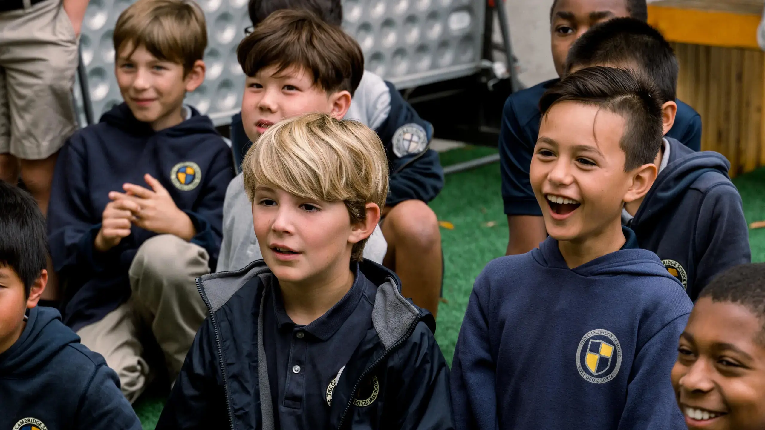 A group of Cambridge School elementary boys are seated together outdoors, displaying joyful and inquisitive expressions.