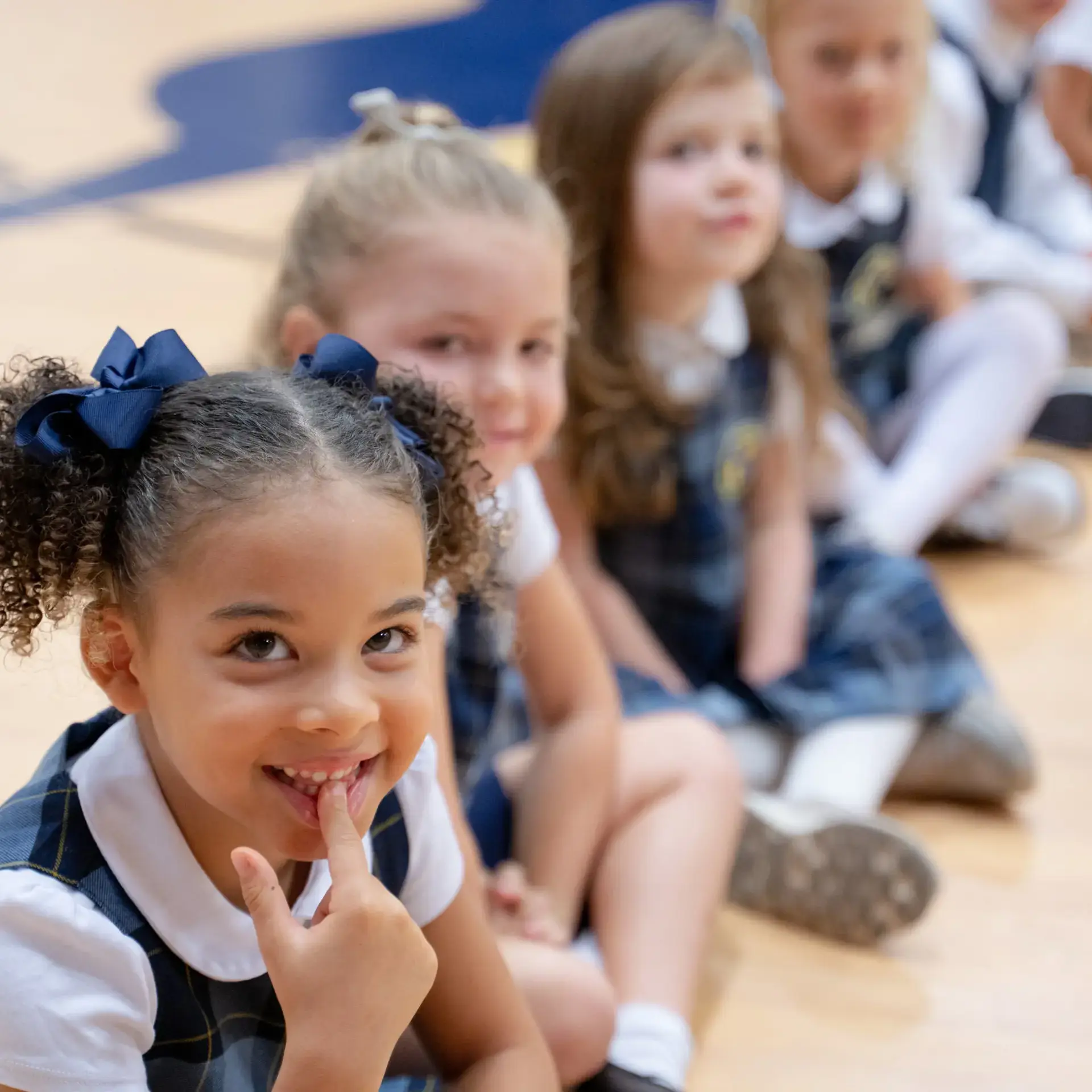 Young students at The Cambridge School dressed in uniforms sit in a line, smiling and preparing for picture day at one of the best private elementary schools in San Diego.