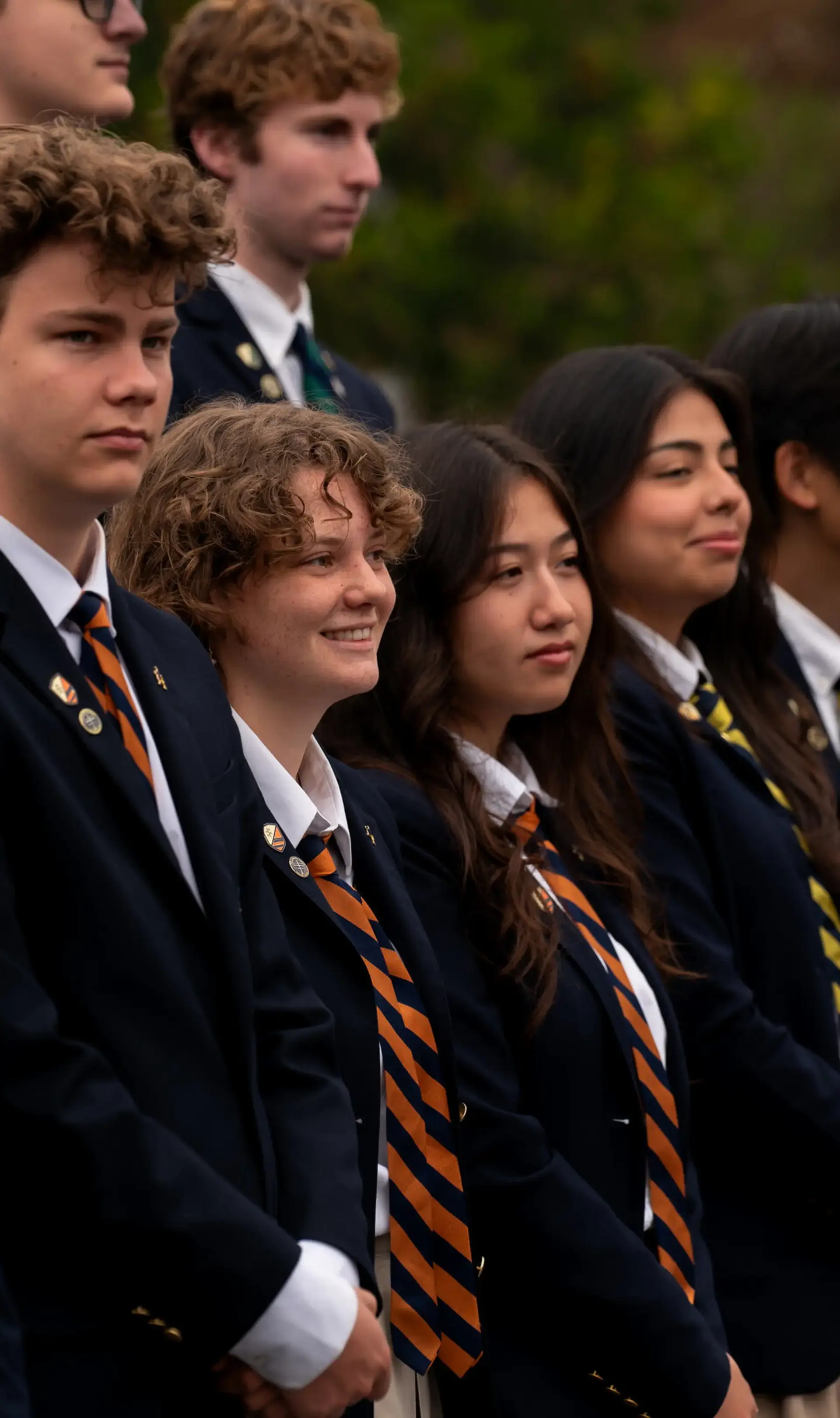 A line of upper school students from The Cambridge School dressed in formal uniforms, standing attentively outdoors during a school ceremony.