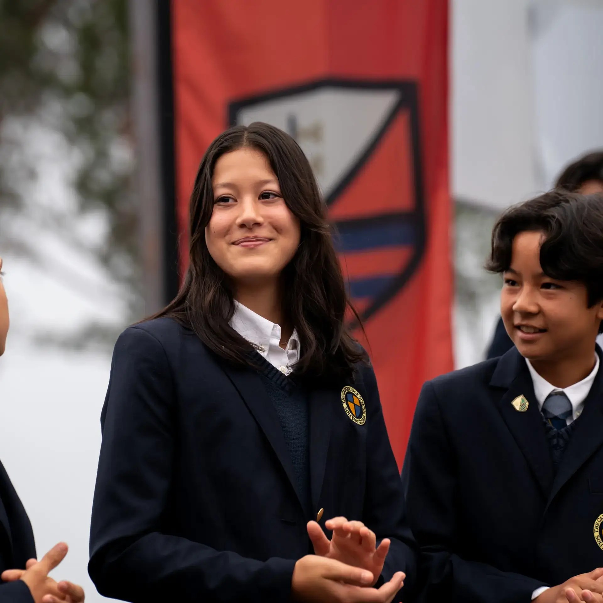Middle school students in formal uniforms stand smiling in front of colorful house banners during a school event at The Cambridge School.