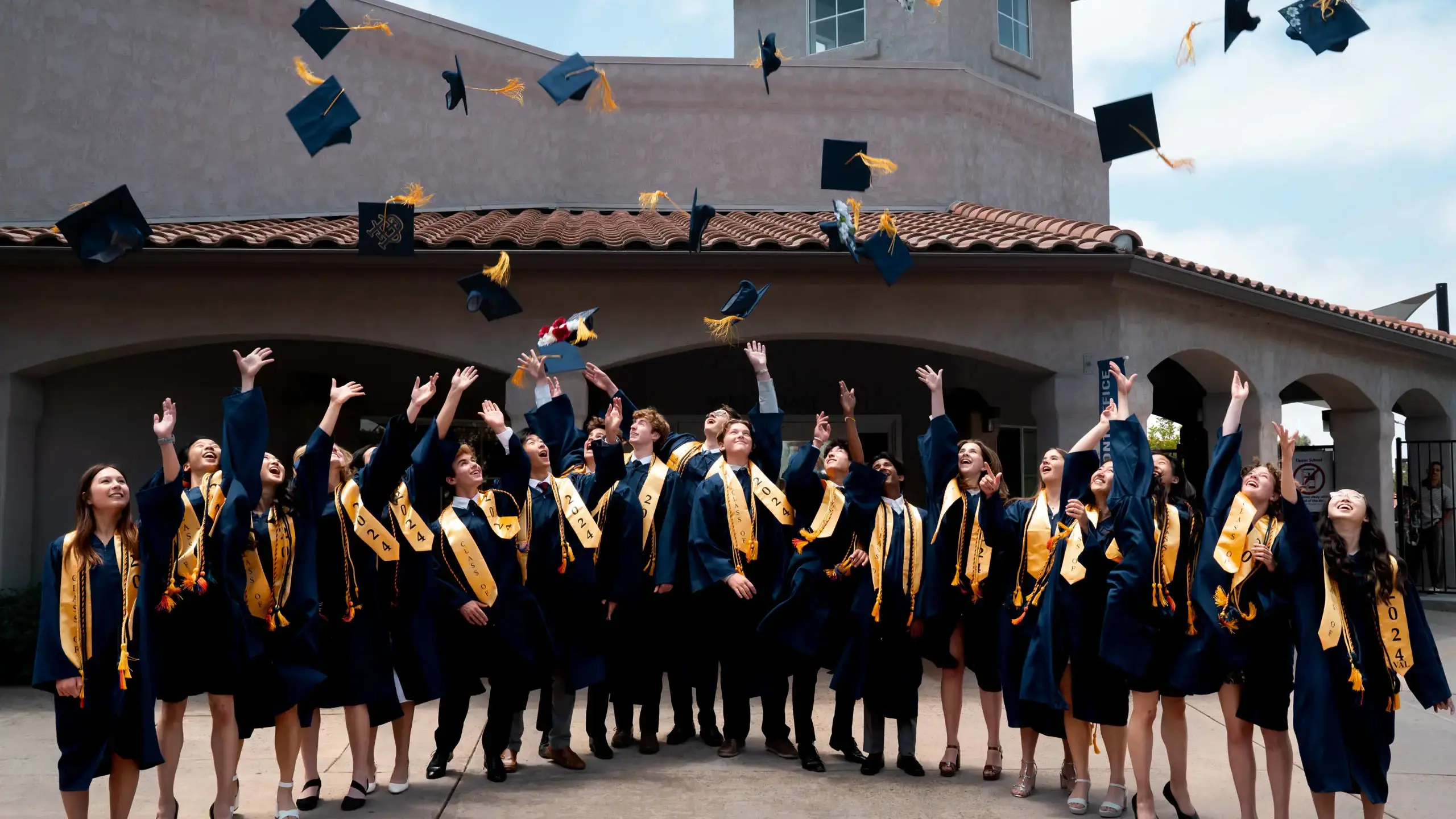 Graduates of The Cambridge School joyfully throw their caps into the air.