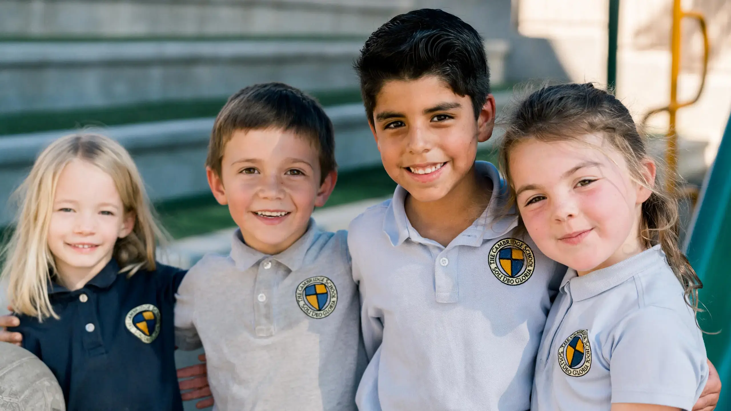 Four diverse and smiling Cambridge School elementary students in uniform stand together.