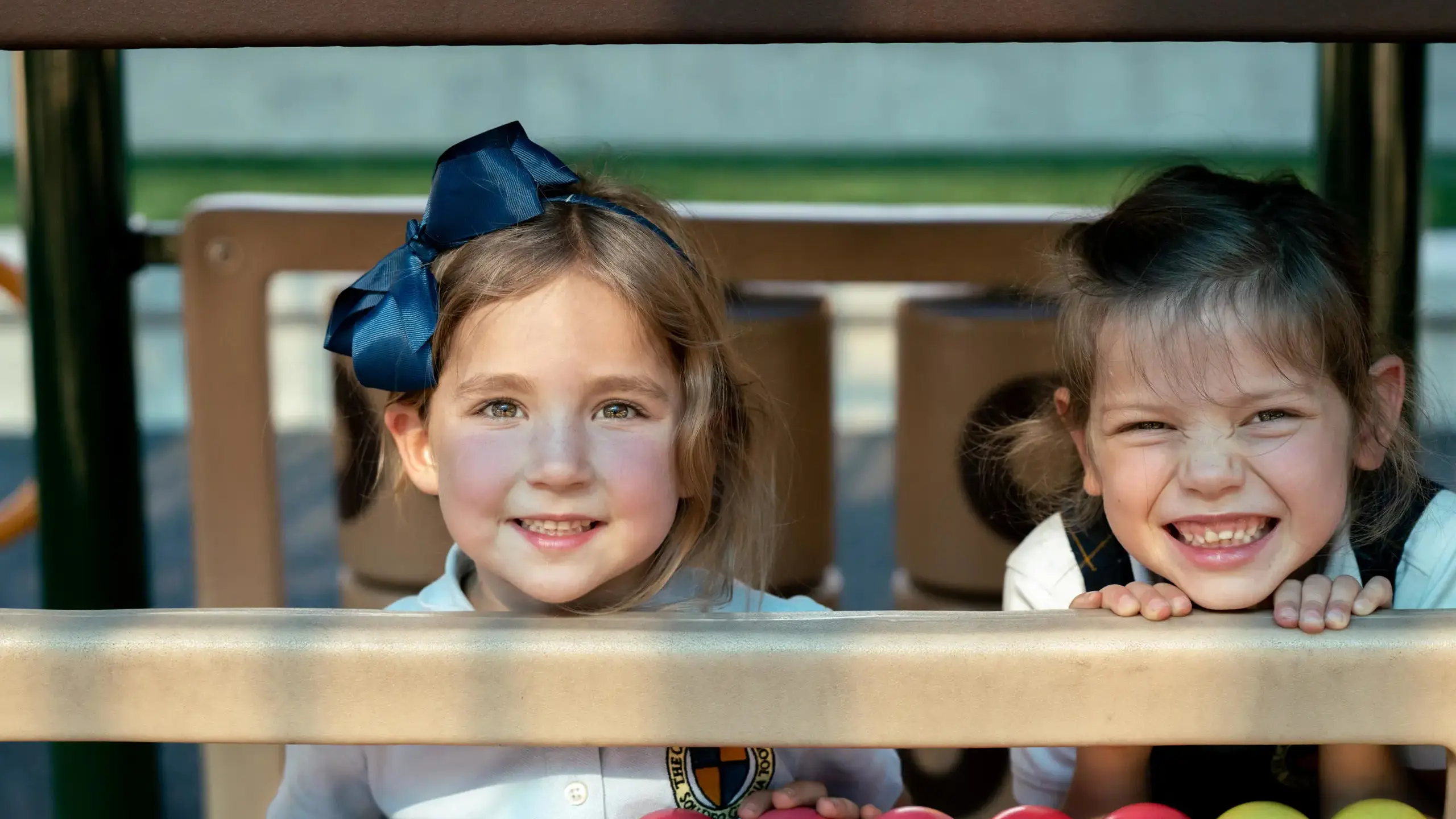 Two joyful Junior Kindergarten students from The Cambridge School smile from a playground, reflecting the program's focus on physical activity, social development, and nurturing the whole child.