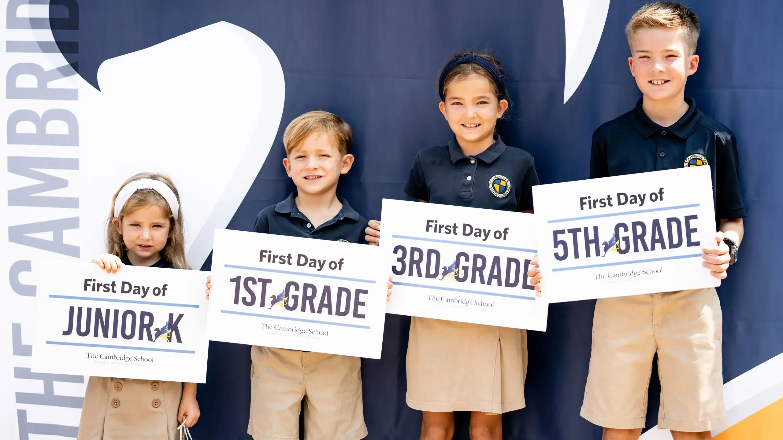 Students at The Cambridge School, a private Christian school in San Diego, smile while holding grade-level signs on the first day of school—representing Junior Kindergarten through 5th grade.