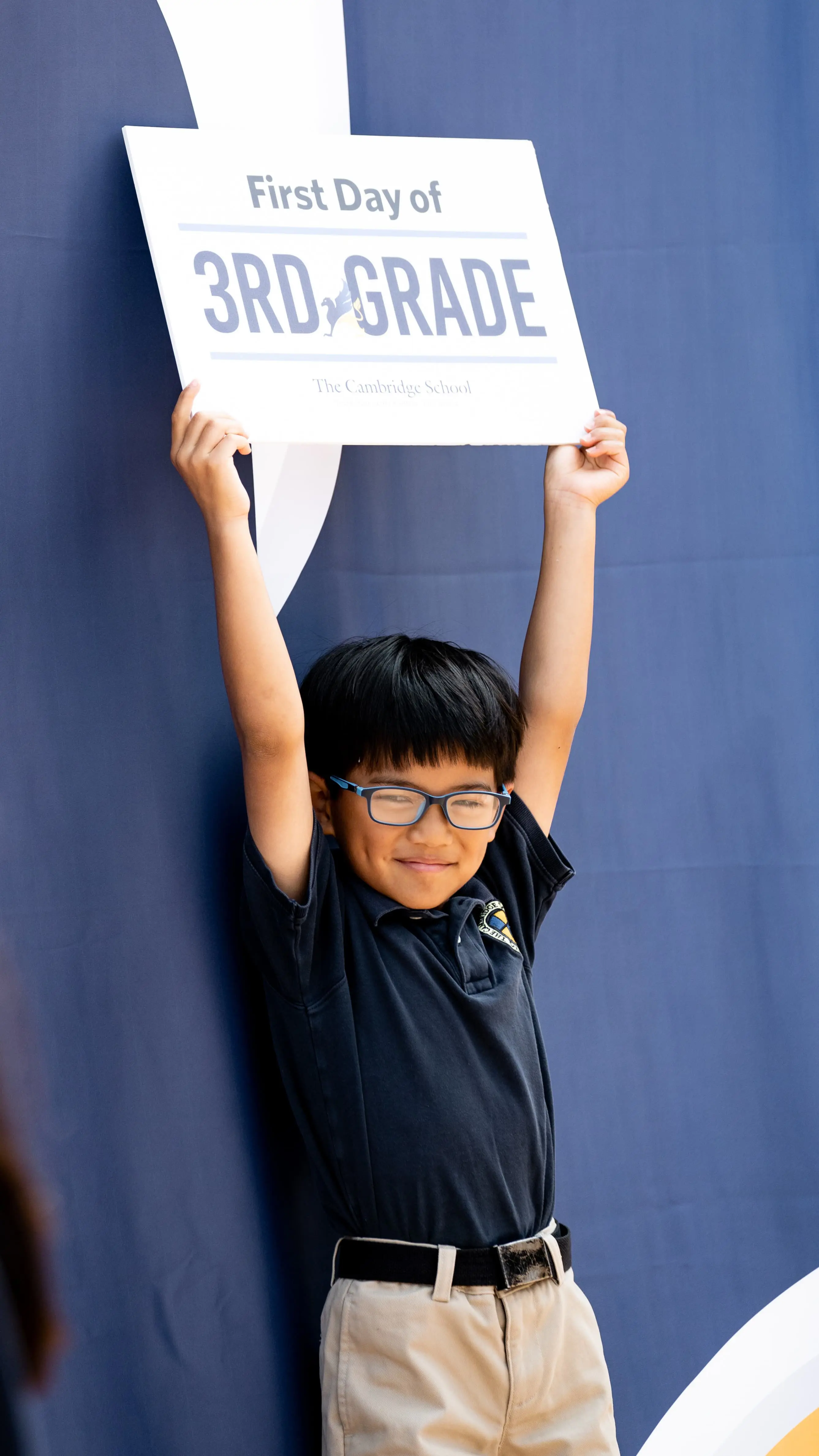 Excited for his first day of school, a bright student at The Cambridge School raises a sign above his head in triumph.