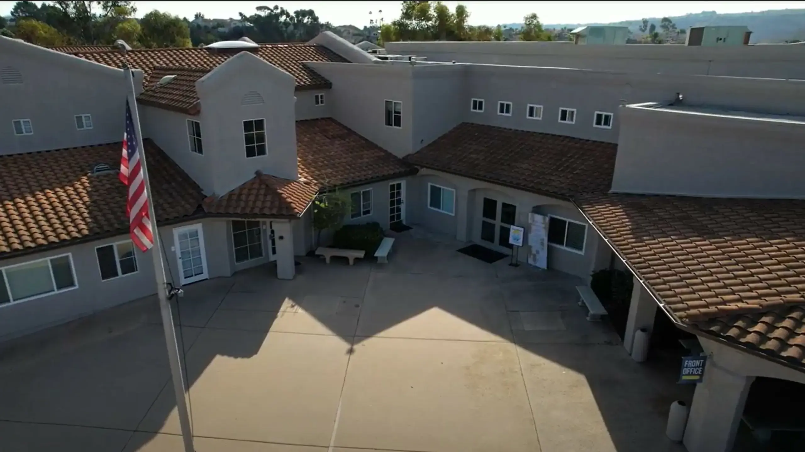 Aerial view of The Cambridge School campus, showcasing its inviting buildings with tiled roofs, a central courtyard, and an American flag.